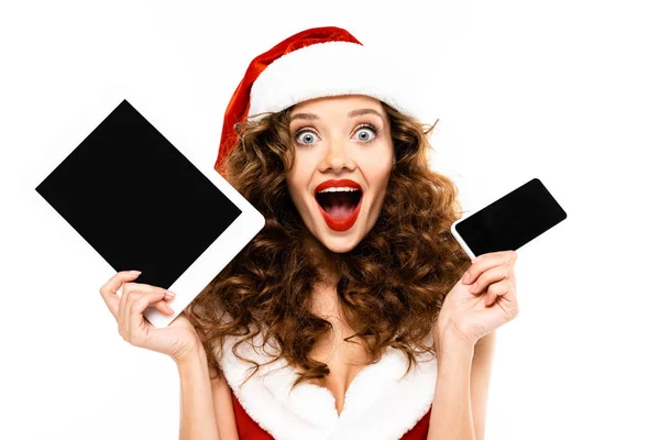Excited curly woman in santa costume holding digital devices with blank screens, isolated on white — Stock Photo