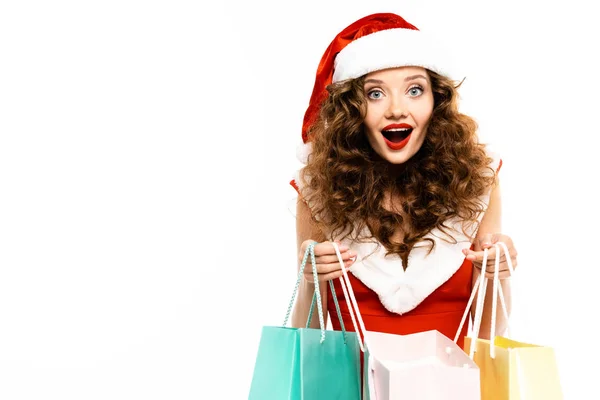 Sorpresa ragazza in costume da Babbo Natale in posa con borse della spesa, isolato su bianco — Foto stock