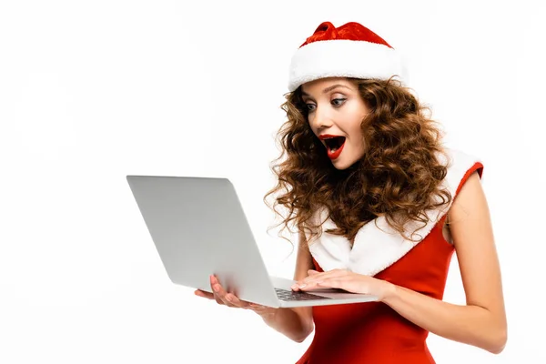 Eccitato ragazza riccia in costume da Babbo Natale utilizzando il computer portatile, isolato su bianco — Foto stock