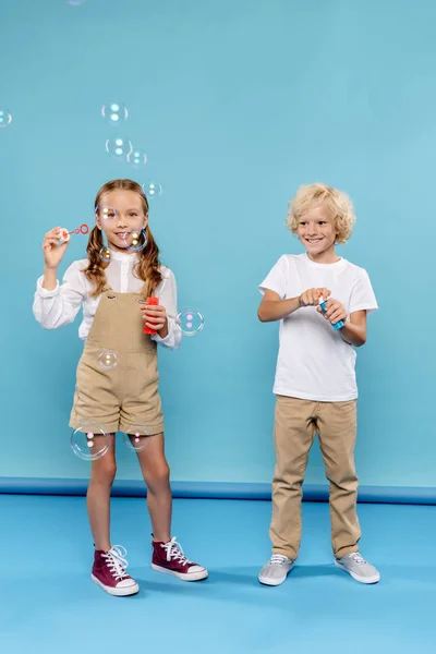 Bambini sorridenti e carini che soffiano bolle di sapone su sfondo blu — Foto stock