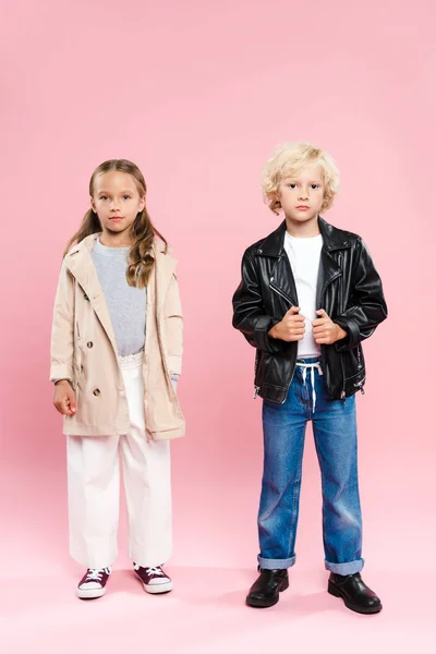 Crianças de casaco e jaqueta de couro olhando para a câmera no fundo rosa — Fotografia de Stock