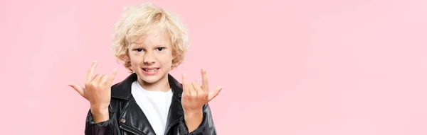 Panoramic shot of smiling kid showing rock sign isolated on pink — Stock Photo