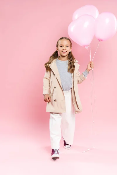 Enfant souriant en tenue d'automne marchant et tenant des ballons sur fond rose — Photo de stock