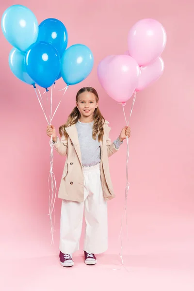 Smiling kid in autumn outfit holding balloons on pink background — Stock Photo