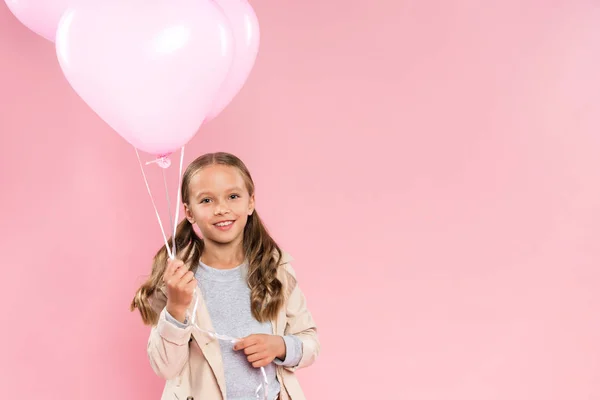 Усміхнена дитина в осінньому вбранні тримає повітряні кулі ізольовані на рожевому — стокове фото