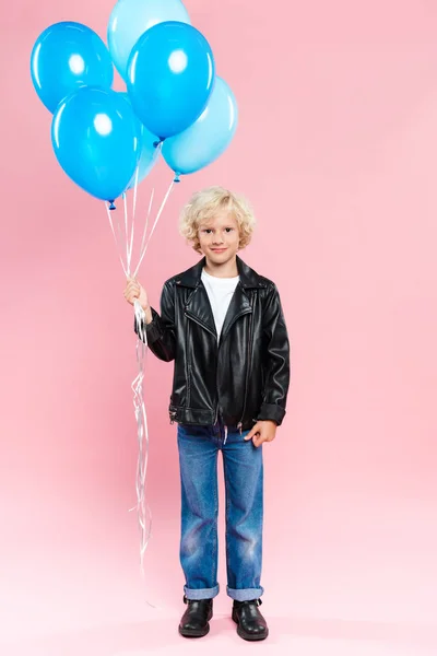 Garoto sorrindo segurando balões e olhando para a câmera no fundo rosa — Fotografia de Stock