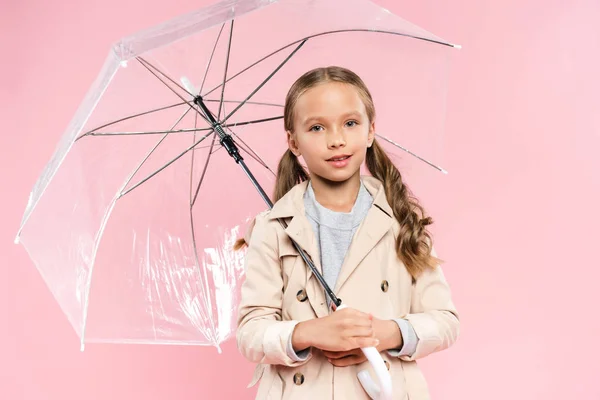 Улыбающийся ребенок в осеннем наряде с зонтиком, изолированным на розовом — стоковое фото