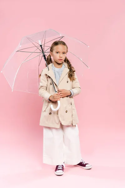 Kind im Herbst-Outfit mit Regenschirm auf rosa Hintergrund — Stockfoto