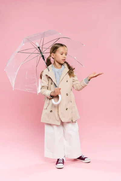 Kid in autumn outfit with outstretched hand holding umbrella on pink background — Stock Photo