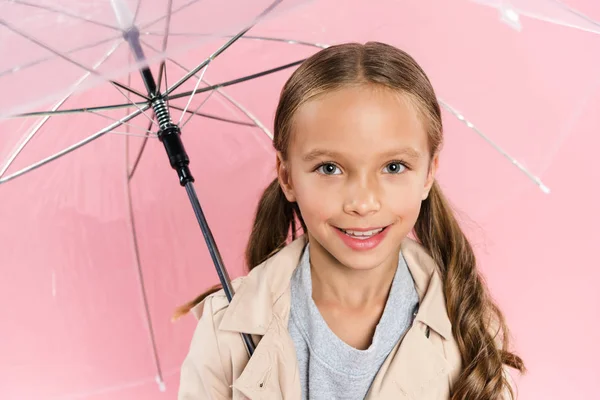 Високий кут зору усміхненої дитини в осінньому вбранні, що тримає парасольку ізольовано на рожевому — стокове фото