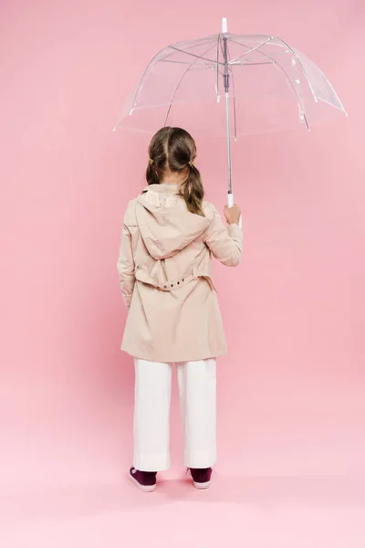 Visão traseira da criança na roupa de outono segurando guarda-chuva no fundo rosa — Fotografia de Stock