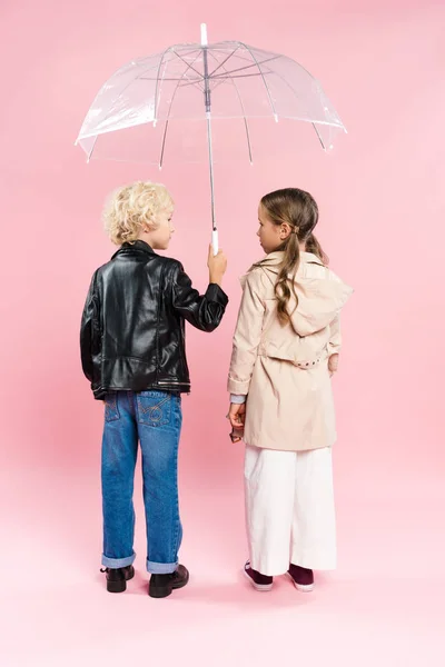 Back view of kids looking at each other and holding umbrella on pink background — Stock Photo