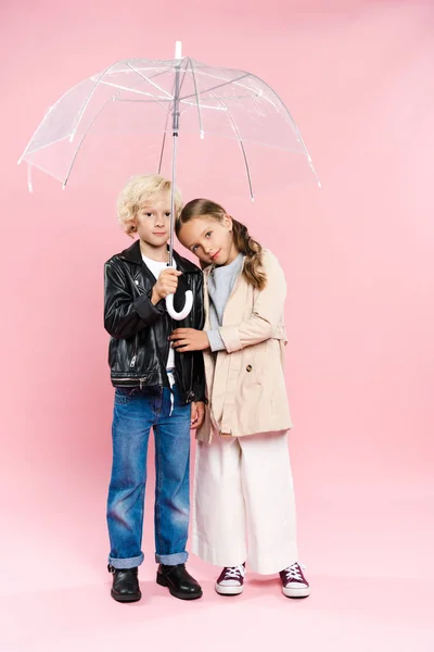 Cute kids hugging and holding umbrella on pink background — Stock Photo