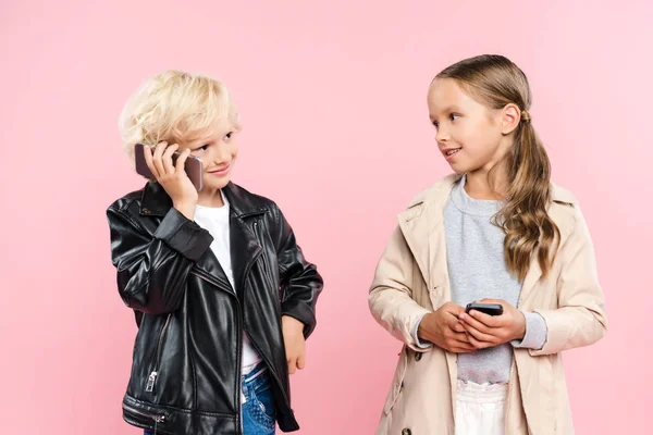 Niños sonrientes y lindos sosteniendo y hablando en el teléfono inteligente sobre fondo rosa - foto de stock