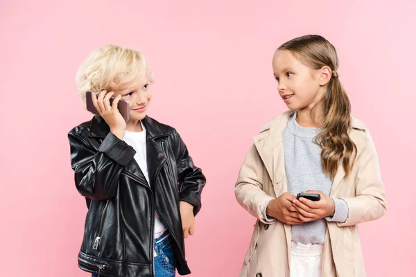 Smiling and cute kids holding and talking on smartphone on pink background — Stock Photo