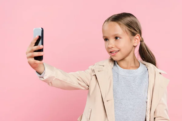 Sonriente y lindo niño tomando selfie aislado en rosa - foto de stock