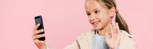 Panoramica colpo di sorridente e carino bambino agitando durante la video chat isolato su rosa — Foto stock