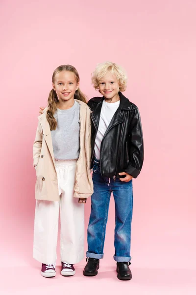 Lächelnde Kinder, die sich umarmen und in die Kamera auf rosa Hintergrund schauen — Stockfoto