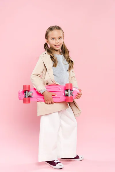 Sorridente e carino bambino che tiene penny board su sfondo rosa — Foto stock