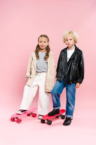 Enfants souriants debout sur le panneau penny sur fond rose — Photo de stock