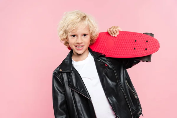 Sonriente y lindo niño sosteniendo penny board aislado en rosa - foto de stock