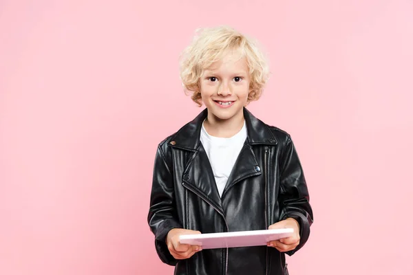 Smiling kid holding digital tablet and looking at camera isolated on pink — Stock Photo