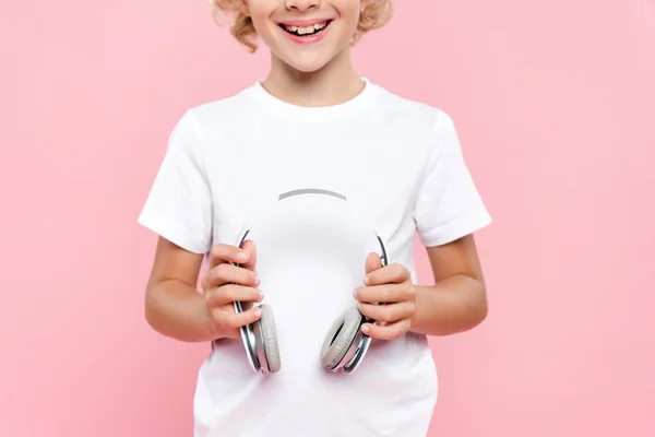 Cropped view of smiling kid in t-shirt holding headphones isolated on pink — Stock Photo