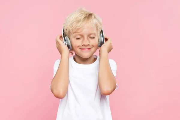 Garoto sorridente com fones de ouvido ouvindo música isolada em rosa — Fotografia de Stock