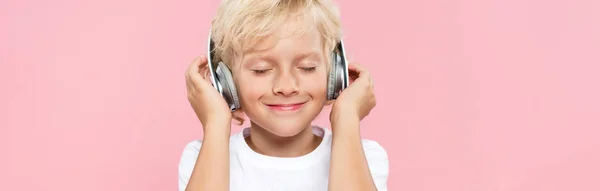 Panoramic shot of smiling kid with headphones listening music isolated on pink — Stock Photo