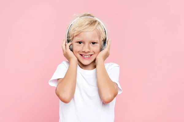 Niño sonriente con auriculares escuchando música aislada en rosa - foto de stock