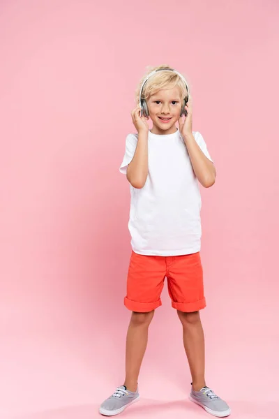 Улыбающийся ребенок с наушниками слушает музыку на розовом фоне — стоковое фото