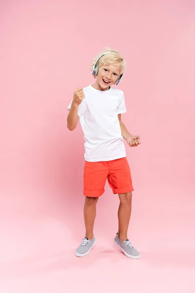 Niño sonriente con auriculares escuchando música y bailando sobre fondo rosa - foto de stock