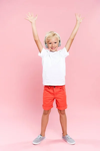 Niño sonriente con las manos extendidas escuchando música sobre fondo rosa - foto de stock