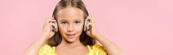 Panoramaaufnahme eines lächelnden Kindes mit Kopfhörern, das isoliert auf rosa Musik hört — Stockfoto