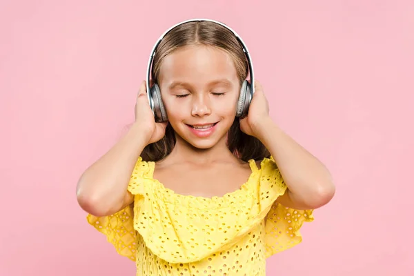 Усміхнена дитина з навушниками слухає музику ізольовано на рожевому — стокове фото