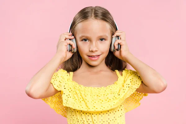 Niño sonriente con auriculares escuchando música aislada en rosa - foto de stock
