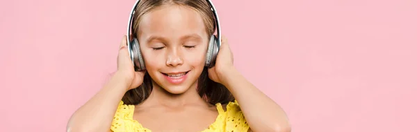 Colpo panoramico di bambino sorridente con cuffie ascoltare musica isolata su rosa — Foto stock