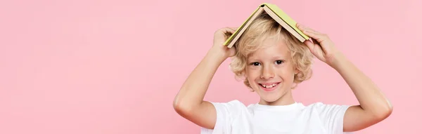 Plano panorámico de niño sonriente sosteniendo libro aislado en rosa - foto de stock