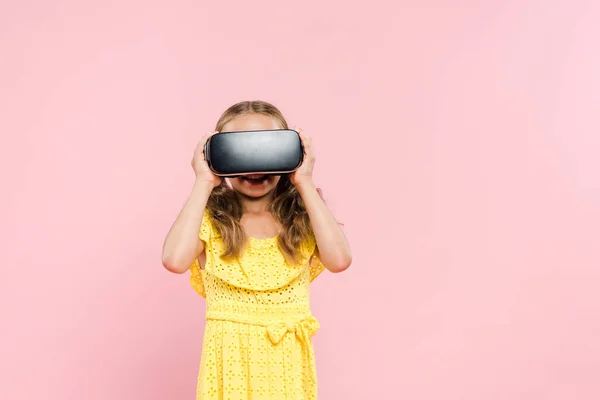 Улыбающийся ребенок с наушниками виртуальной реальности, изолированными на розовом — стоковое фото