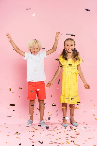 Улыбающиеся дети с протянутыми руками рядом падающие конфетти на розовом фоне — стоковое фото