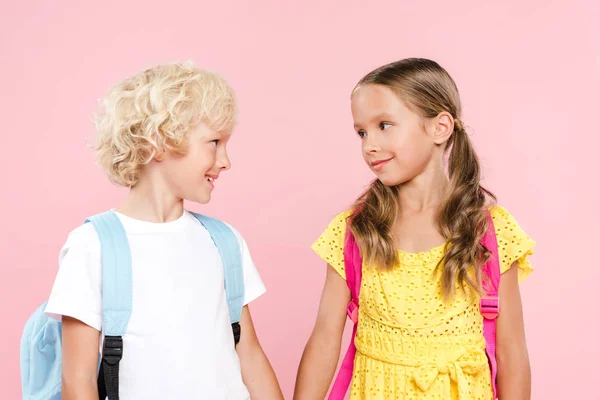 Crianças em idade escolar sorridentes com mochilas olhando umas para as outras isoladas em rosa — Fotografia de Stock