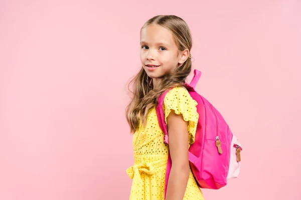 Усміхнена школярка з рюкзаком дивиться на камеру ізольовано на рожевому — стокове фото