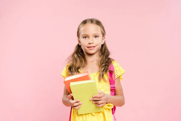 Lächelndes Schulmädchen mit Rucksack, der Bücher isoliert auf rosa hält — Stockfoto