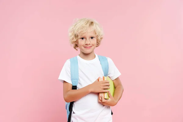 Smiling schoolboy with backpack holding books isolated on pink — Stock Photo