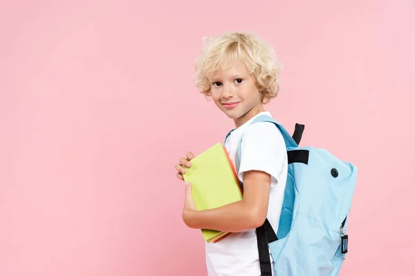 Lächelnder Schuljunge mit Rucksack, Buch isoliert auf rosa — Stockfoto