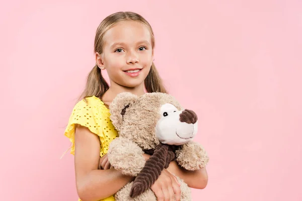 Bambino sorridente guardando la fotocamera e tenendo orsacchiotto isolato su rosa — Foto stock