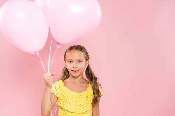 Улыбающийся и милый ребенок держит воздушные шары на розовом фоне — стоковое фото