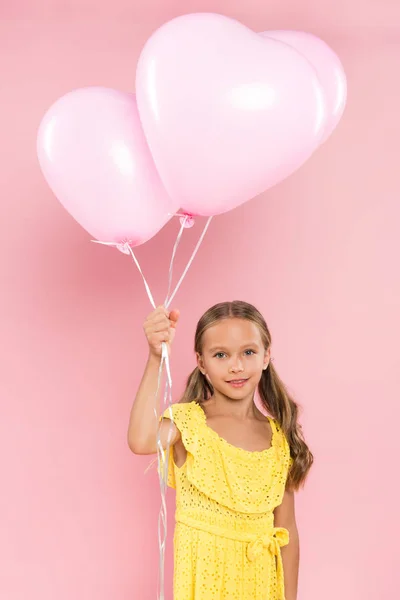 Bambino sorridente e carino che tiene palloncini su sfondo rosa — Foto stock