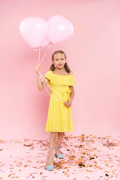 Bambino sorridente e carino che tiene palloncini su sfondo rosa — Foto stock
