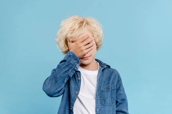 Müde und niedliche Kind verdeckt Gesicht isoliert auf blau — Stockfoto